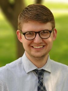 Chad Iwertz headshot wearing black glasses, white shirt, and a tie